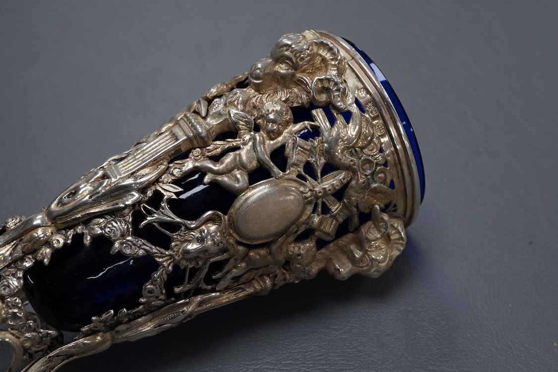 A late Victorian continental pierced silver posy vase, with blue glass liner, decorated with cupids, ram's heads and birds, on tripod supports with hoof feet, import marks for William Moering, London, 1898, height 15.2cm